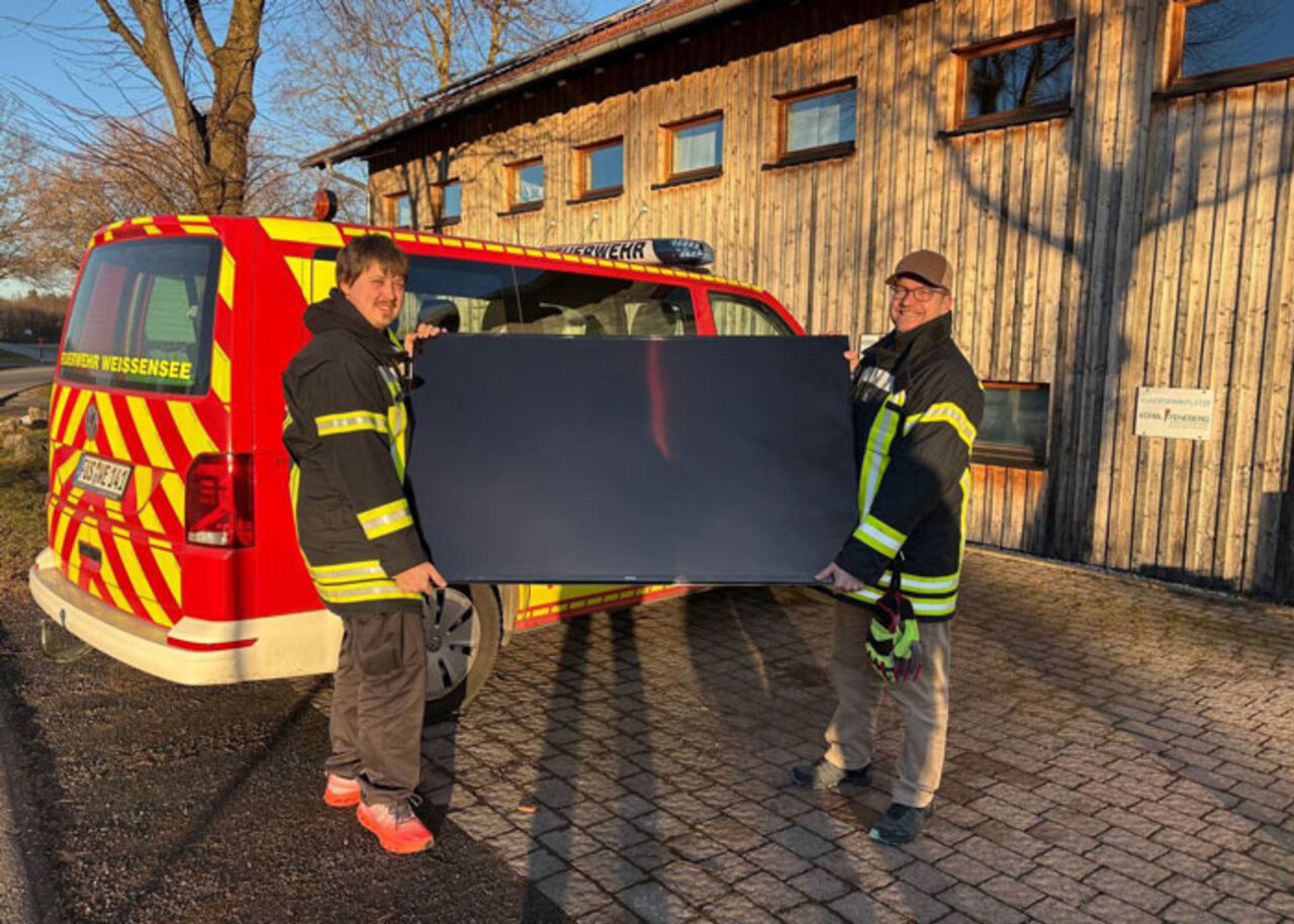 Feuerwehrleute der FW Weissensee tragen einen neuen Großbildmonitor